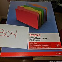 Close-up view of Staples brand box showing assorted color 3-tab heavyweight file folders, letter size, 50 count.