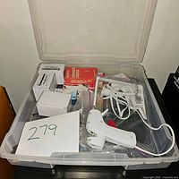 Clear plastic bin from above showing various office supplies like tape gun, staples, paper clips and boxes.