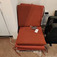 Pile of four outdoor cushions: two backrest cushions and two seat cushions in rust-orange fabric with ties.