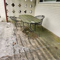 Photo of outdoor wrought iron oval table with glass top and 2 matching chairs on patio, showing overall condition and environment.