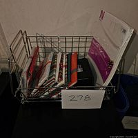 Photo showing a metal basket containing various packages of photo paper and some loose sheets.