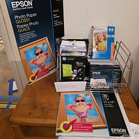 Epson and HP photo printer paper packs arranged in metal rack and on table showing various sizes and packaging.