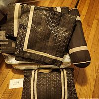 Queen duvet set folded on floor showing geometric patterns and beige trims with bolster pillows on top.