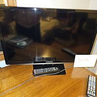 Front view of Samsung flat screen TV on wooden table with Samsung remote on the base.