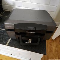 Closed view of black Sentry Safe steel lockbox with key in lock on front.