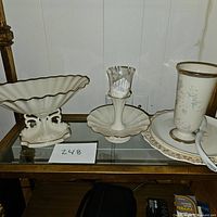 View of the three porcelain serving pieces: a large scalloped serving plate on an ornate base, a compote dish on a pedestal holding a glass tumbler, and a tall cylindrical vase on a matching saucer.