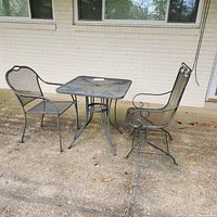 Outdoor square metal mesh table with two matching metal mesh chairs on concrete patio in front of brick wall