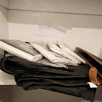 Shelf with black fabric suit bags stacked along with white fabric bags, some new and some used.