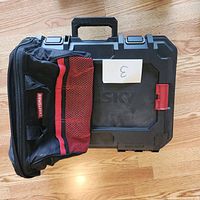 Craftsman black and red fabric tool bag next to Husky hard case on wooden floor