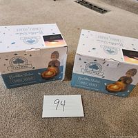 Two Buddha Statue Candle Holder boxes placed side by side on carpet with label '94' in front. The boxes show the brand 'OakiWay' and depict the product image of the Buddha candle holder.