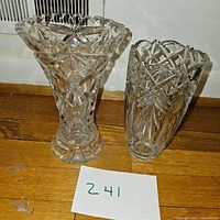 Two clear cut glass vases side by side on wooden floor with measurement tape shown for the taller vase