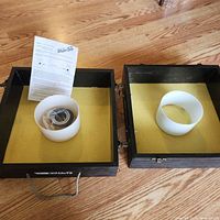 Two black wooden boxes with yellow inner surface, one with metal ring, one with white plastic ring, washers inside one box, and printed instructions.