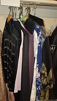 Side view of assorted women's clothing on hangers including dark jacket, light pink blouse, purple top, black garment, and floral blouse.