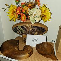 Wooden vase with artificial flowers and two carved wooden figurines on display