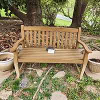 Full view of sturdy wooden garden bench situated outdoors with floral carving on backrest.