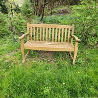 Full view of wooden garden bench on grass showing armrests, vertical slat backrest, wooden seat slats, and natural outdoor setting.