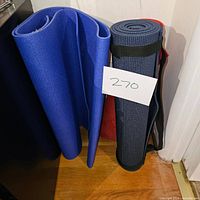 Three yoga mats: blue mat folded, black mat rolled with black carrying strap, red mat rolled with floral design