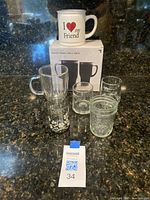Photo showing two heated travel mugs with 'I Love My Friend' design on top of their retail box, along with several small clear shot glasses in front.