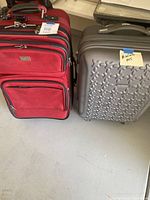 Two small suitcases side by side: red fabric suitcase and gray hard-shell suitcase.