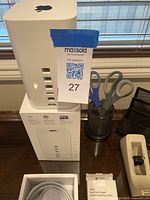 Photo showing Apple AirPort Extreme wireless router sitting on its original box with MaxSold lot card attached.