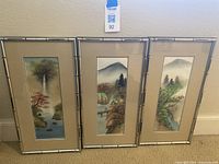 Three framed Asian style pictures featuring natural landscapes with mountains, water, and trees, in bamboo-style frames.