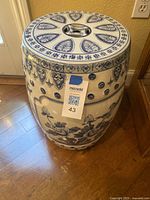 Front angle view of the blue and white ceramic garden stool showing floral pattern on the side and geometric motifs on the top surface.