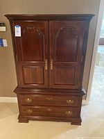 Front view of closed Broyhill wooden armoire cabinet showing two upper doors with ornate handles and two lower drawers with matching handles.