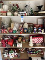 Full view of three shelf cabinet filled with assorted Christmas figurines, candles, vases and boxes