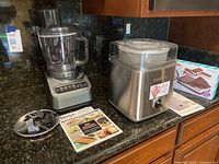 Ninja BN 600 food processor with disc attachment and user manual next to Cuisinart ICE-30 ice cream maker on kitchen counter.