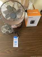 Front view of retro-style metal fan next to GeekHeat electric heater box, showing cables and tags.