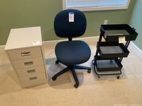 Blue fabric office chair, black metal rolling cart, white filing cabinet side by side in room under window.