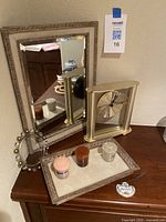 Photo of the mantel clock, mirror, tray, candles, and metal circular object on a wooden surface