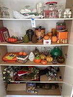 Full view of cabinet with shelves filled with glassware, pumpkin ornaments, seasonal figurines, and wreaths.