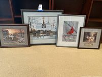 Four framed pictures side-by-side on the floor including two larger scenic paintings, one smaller rustic scene and one cardinal photograph.