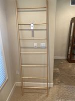 Front view of the natural wood quilt ladder showing 7 rungs and overall height and width, placed against a wall near a window.