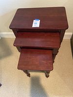 Three wooden nesting tables stacked with the largest on top, showing smooth rectangular tops and turned legs.