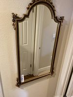 Full view of the ornate gold wall mirror mounted on a textured beige wall.