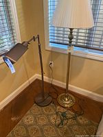 Two floor lamps side by side in a corner, one modern adjustable bronze lamp with cylindrical shade and one classic bronze lamp with pleated shade.