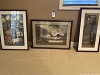 Photo showing all three framed art prints together on the floor: house and flower scene, ocean landscape, and interior stairway scene.
