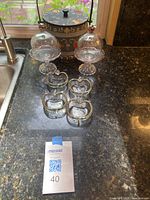 Photo showing two large dome glass dishes with pedestal bases and lids, and five smaller apple-shaped dishes on a kitchen counter.