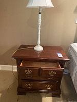 Single dark brown wooden nightstand shown with open top drawer and white lamp on top