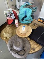 Photo showing three hats, blue backpack, sunglasses, sprayed can, and part of a red pouch on table