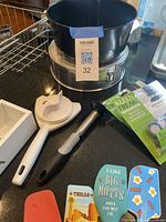 Photo showing black springform pan, white plastic measuring tool, black kitchen tool, decorative spatulas, and green label packet