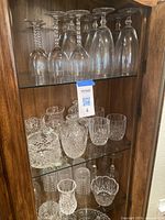 Full cabinet view showing an assortment of stemmed glasses on top shelf and various cut crystal pieces including pitchers, bowls, and glasses on lower shelves.
