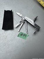 Multi-tool cutter partially opened showing knife blade, saw blade, corkscrew, bottle opener, screwdriver and other tools with black pouch case on the left