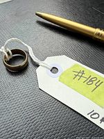 Yellow 10K gold band on black textured background next to gold pen and tag