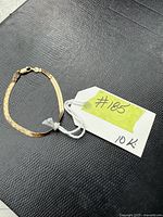 Full view of flat 10K gold herringbone chain bracelet on black textured surface with tag labeled #185 10K