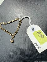 Bracelet laid flat on textured black surface showing chain and basket charm