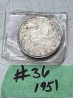 Photo of 1951 Canadian silver dollar coin in protective plastic holder, showing reverse side with canoe design and inscriptions.