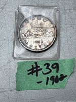 Photo of a 1962 Canadian Silver Dollar coin in a plastic protective sleeve with a green label marked '#39 - 1962'.